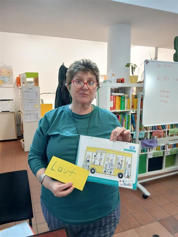 Frau hält Bild von Bus und Zettel mit Aufschrift "laut" in der Hand