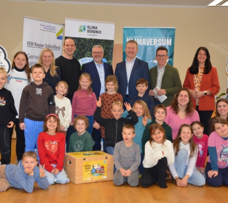 Gruppenfoto von 15 Kindern im Volksschulalter und 7 Erwachsenen mit der Klimakiste und den Pappfiguren der Ausstellung