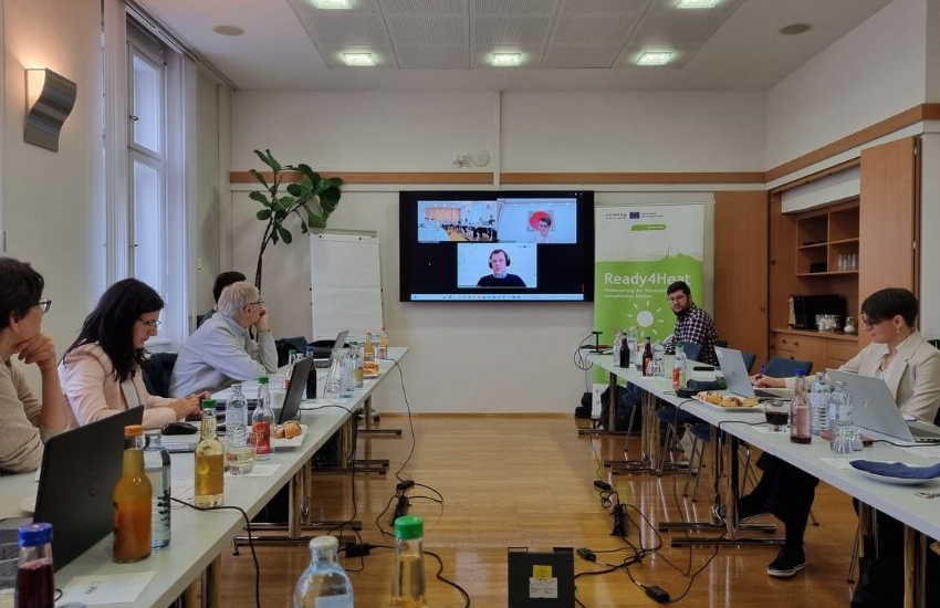Menschen sitzen in U-Form an Tischen und sehen frontal auf Webinar Projektionsfläche
