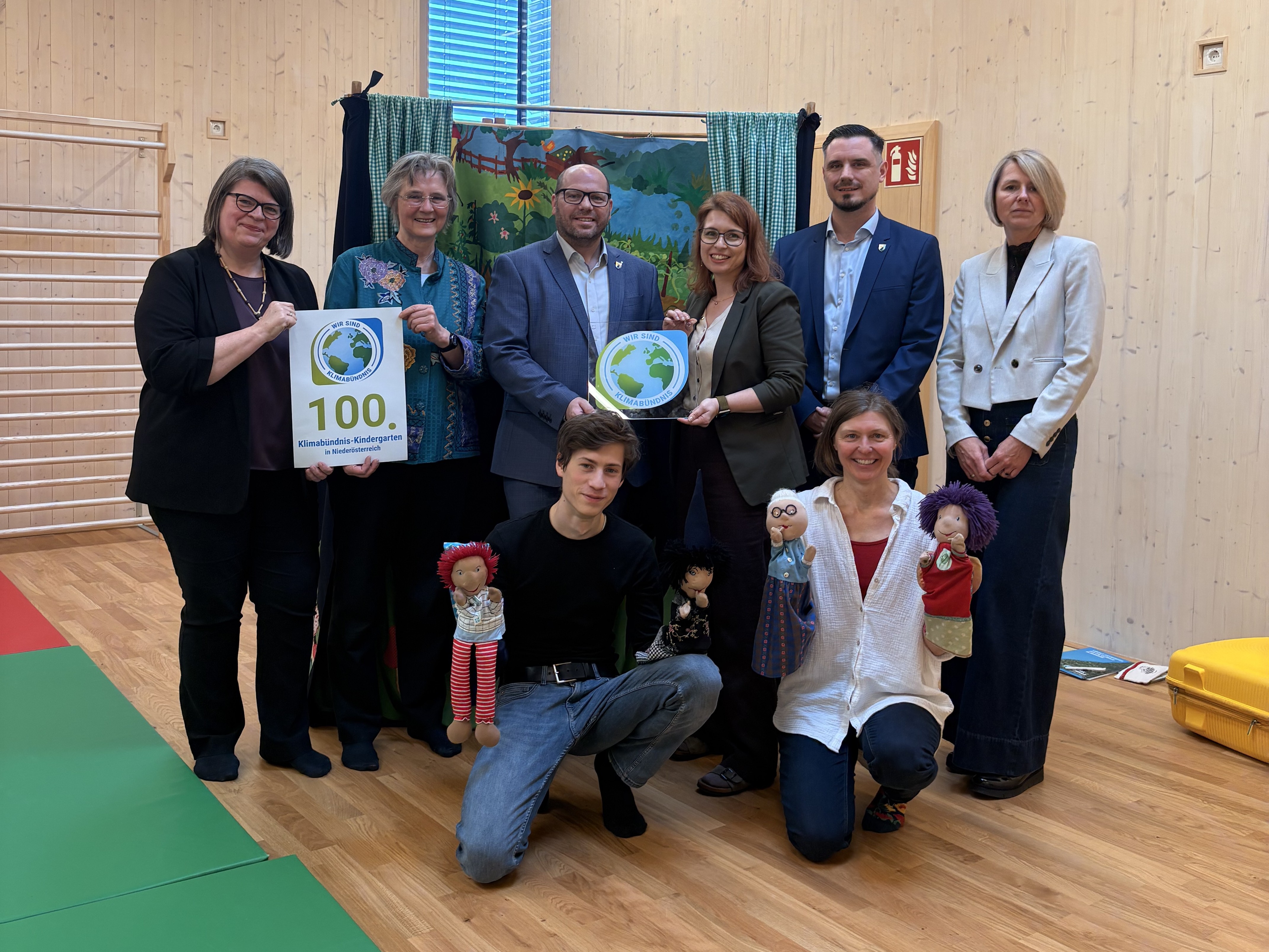 Gruppenbild fünf Frauen und drei Männer mit Klimabündnistafel, 100. Klimabündnis Kindergarten Urkunde und Handspielpuppen