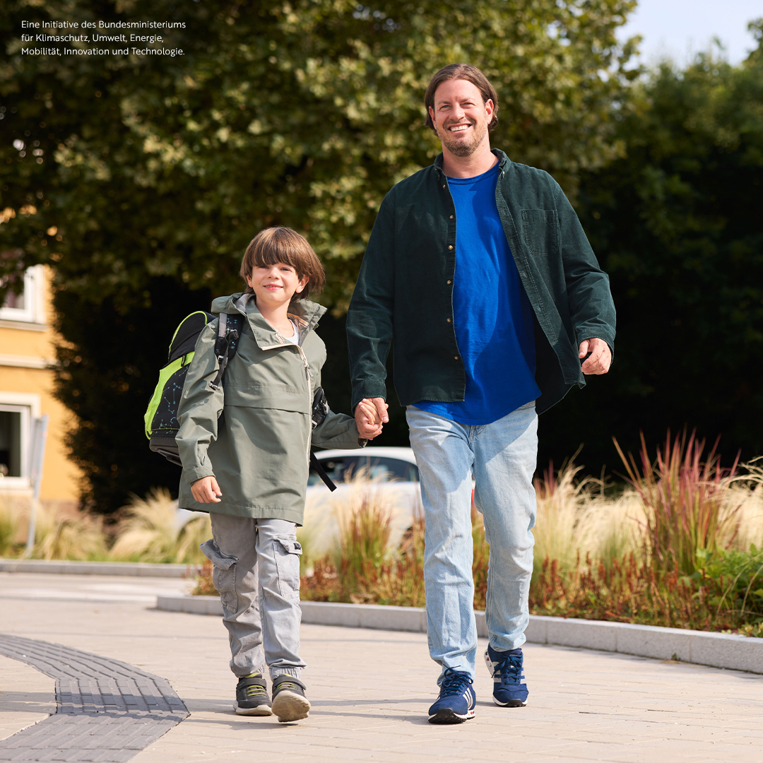 Vater und Sohn spazieren auf einem Fußgängerweg, der Sohn trägt eine Schultasche